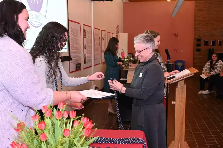 Tri-Alpha eboard President Jessica Aurigemma presents staff inductee, Corrine Armstrong with her cords