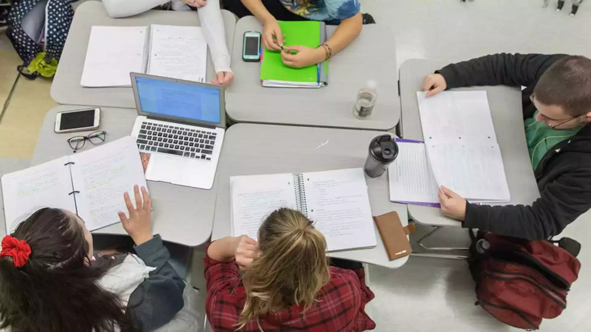 view from above of people working at a workspace covered in notebooks, binders and a laptop